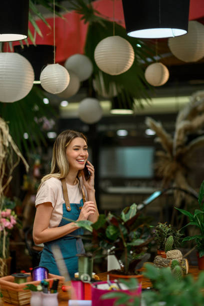 floristería hablando con el cliente en el teléfono inteligente y tomando un pedido en una floristería - florist telephone flower business fotografías e imágenes de stock