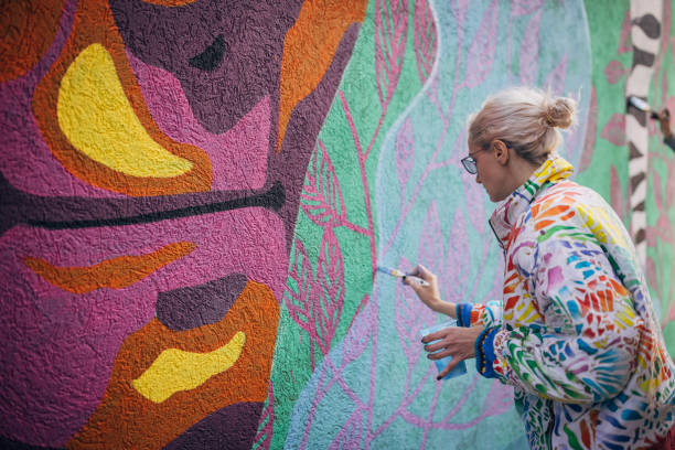 Female artist painting on wall One woman, young female street artist painting on a building wall outdoors. paintings stock pictures, royalty-free photos & images