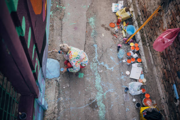 One woman, young female street artist painting on a building wall outdoors.