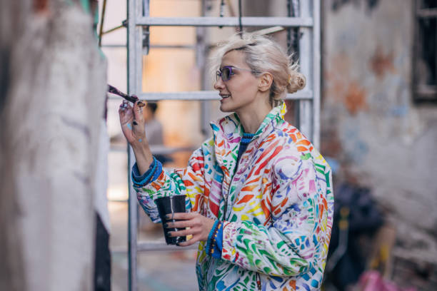 One woman, young female street artist painting on a building wall outdoors.