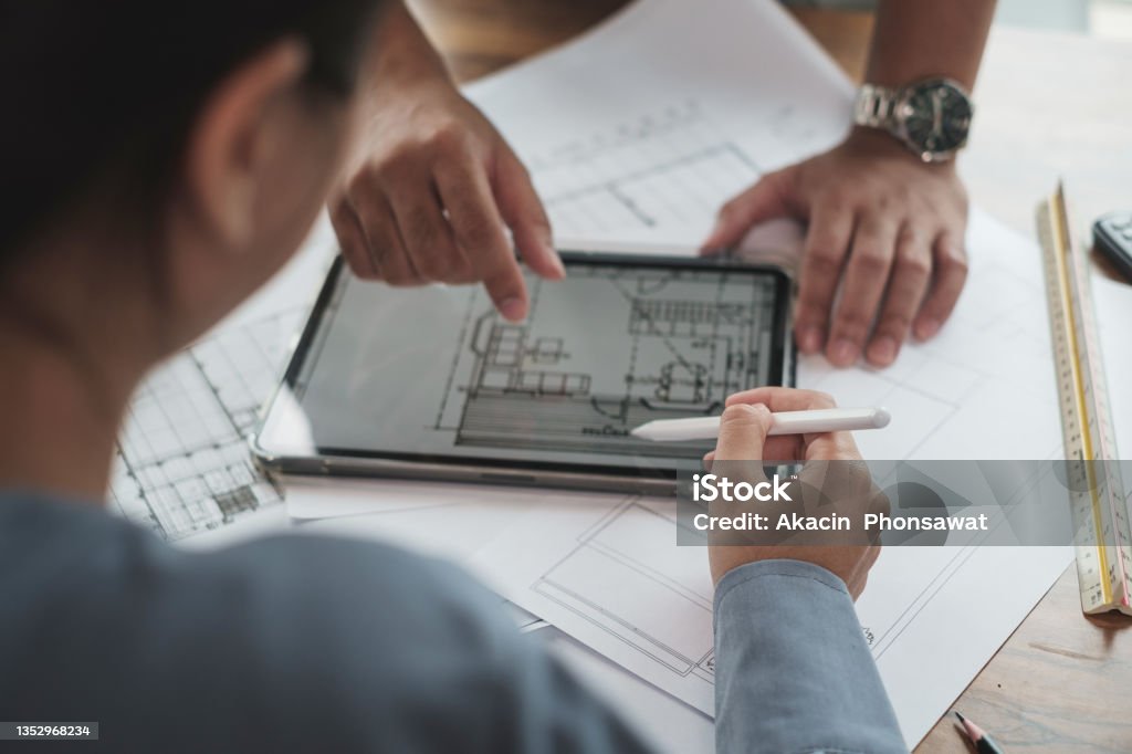 Architect or Engineer team designer discussing detail drawing on digital tablet. Selective focus hand holding pencil. Architect or Engineer team designer discussing detail drawing on digital tablet. Building Information Modeling Stock Photo