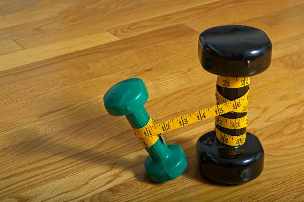 istock Two standing dumbbells, wrapped in measuring tape with light weight leaning away 1352973414