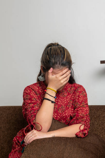 young indian girl getting sad, covering her face because of sadness. a girl crying while sitting on the couch. - blue vertical color image photography imagens e fotografias de stock