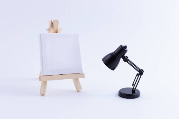 istock Wooden Easel Miniature with Blank White Square Canvas and Table Lamp 1352987686