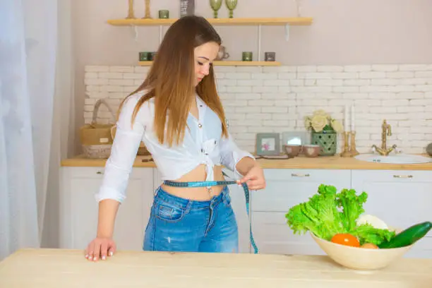 Photo of happy slender woman measures her waist with a tape. vegetarianism, weight loss, dietetics and healthy lifestyle