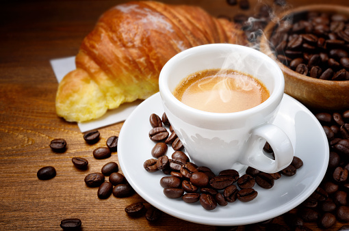 Spresso humeante y croissant con granos de café sobre fondo de madera, primer plano. photo
