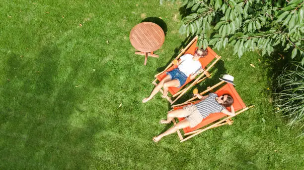 Young girls relax in summer garden in sunbed deckchairs on grass, women friends have fun in green park, aerial top view from above