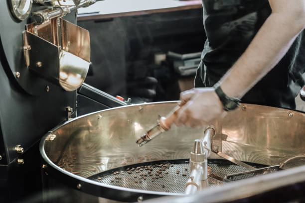 hombre vertiendo granos de café en la máquina tostadora. granos de café oscuros y aromáticos - roasted machine bean mixing fotografías e imágenes de stock