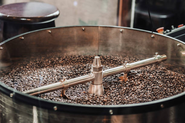 свежеобжаренный кофе. процесс обжарки кофейных зерен на заводе - roasted machine bean mixing стоковые фото и изображения