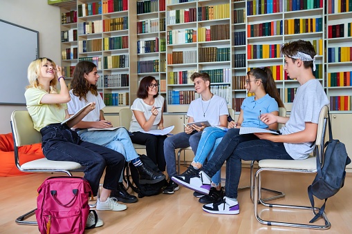 Group of teenagers with middle aged female teacher at library, sitting talking discussing. Education, lesson, youth, teaching, high school, teamwork, college concept.