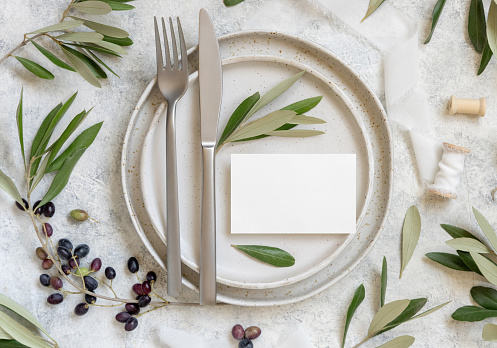 Wedding Table place with place card and porcelain plates decorated with olive branches top view. Elegant modern template with horizontal blank paper card flat lay. Mediterranean mockup, copy space