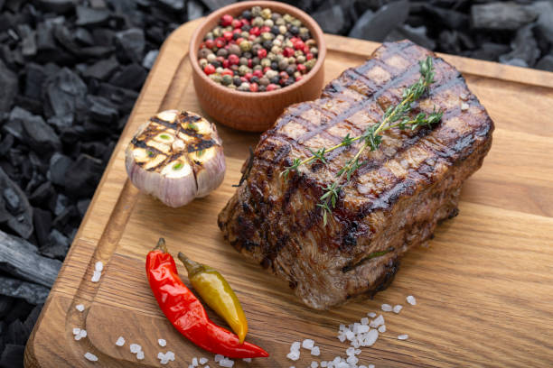 Piece of cooked rump steak with spices served Piece of cooked rump steak with spices served on wooden cutting board roasted stock pictures, royalty-free photos & images