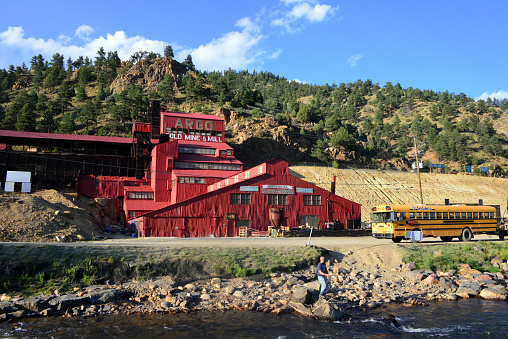 Idaho Springs, Clear Creek County, Colorado, USA: the historic Argo Gold Mine and Mill, built between Clear Creek and the mountains, an intact gold mill built at the entrance of the Argo Tunnel - Riverside Drive with a school bus and an angler on Clear Creek.