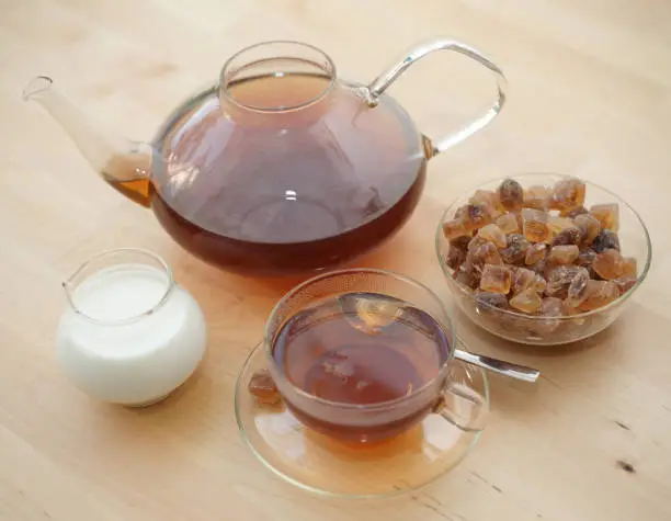 Photo of Black tea in a glass with milk in a pot and rock candy sugar