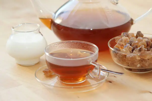 Photo of Black tea in a glass with milk in a pot and rock candy sugar