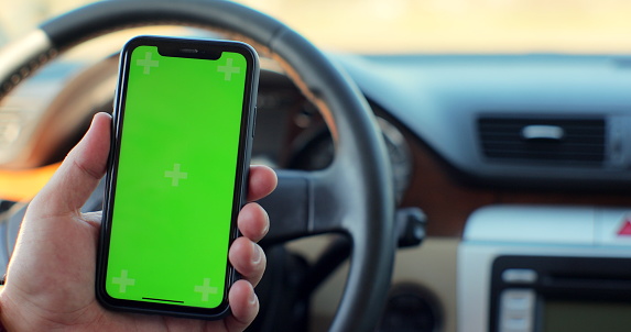 View of man hand holding green screen smart phone in the car. Mockup touchscreen. internet searching