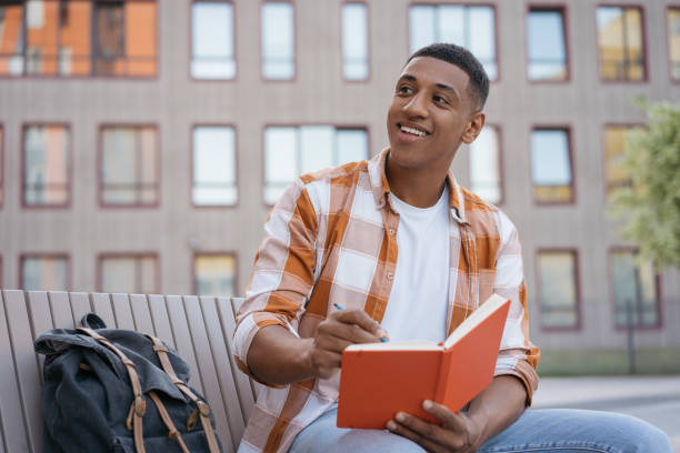 istock Smiling American student studying, taking notes,  exam preparation sitting in university campus looking away. Education concept 1353041700