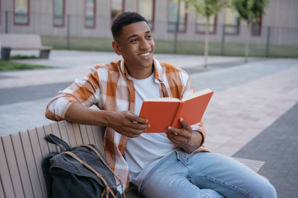 istock African American student studying, learning language sitting in university campus, education concept. Handsome man reading book, relaxing in park 1353041707