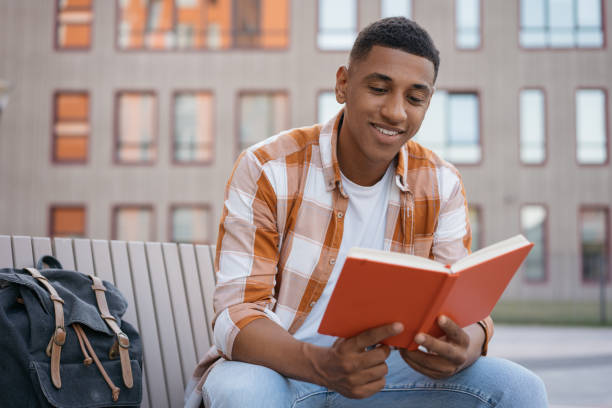 istock Handsome man reading book, relaxing in park. Smiling confident African American student studying, learning language sitting in university campus, education concept 1353041709