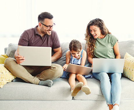 father, mother and daughter having fun doing homework with laptop at home
