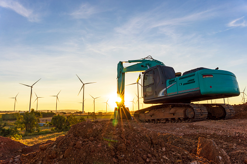 Backhoe and wind turbines that are generating electricity in the background, the concept of sustainable resources, Beautiful sky with wind generators turbines, Renewable energy.