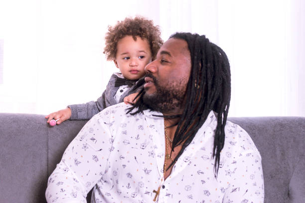 istock Man with dreadlocks talking to his son sitting on the sofa. 1353051623
