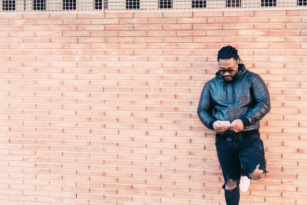 istock Dark-skinned man leaning on the wall while looking at the phone. 1353052230