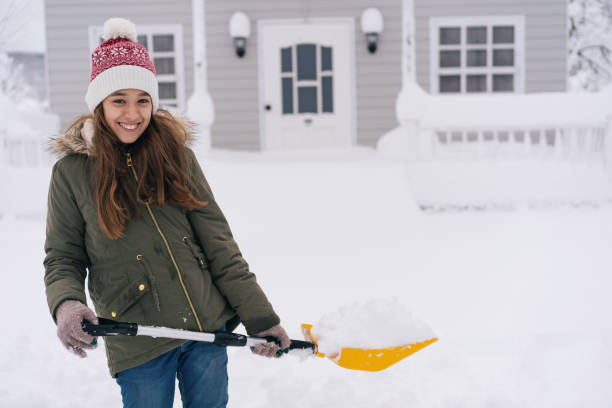 retrato de una niña sonriente, sosteniendo una pala de nieve frente a un porche nevado en un día de invierno. - thick snow fotografías e imágenes de stock