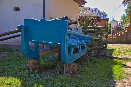 An old blue wooden sleigh stands on logs near a rural house.
