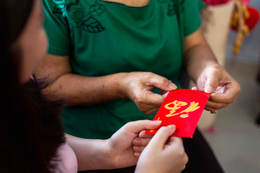 close-up shot of Chinese New Year unrecognizable girl receiving red envelopes from elderly
