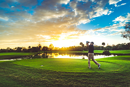 Man on a beautiful scenic sunset golf course swings a golf club
