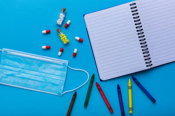 Colored crayons with a protective face mask as a symbol of back to school in pandemic time with a notebook for remarks and rules. School education with the prevention of coronavirus infection.