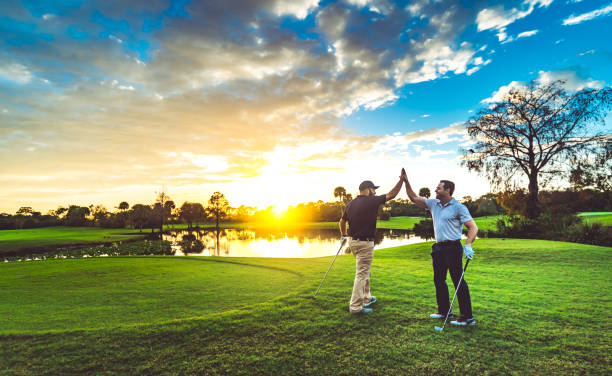 dos golfistas masculinos de cinco en un pintoresco campo de golf al atardecer - golf fotografías e imágenes de stock