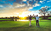 Two male golfers high five on a scenic sunset golf course