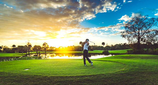 uomo su un bellissimo campo da golf panoramico al tramonto oscilla una mazza da golf - golf playing teeing off men foto e immagini stock