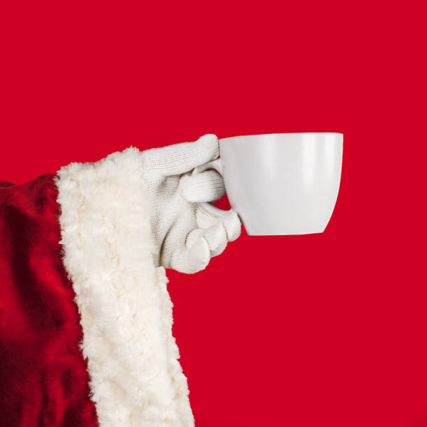 istock Santa Claus hand holding a large tea mug on a red background with space for text or numbers 1353063542