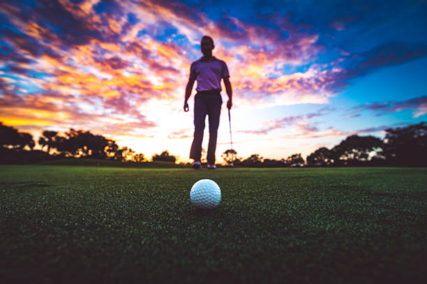 istock Golf ball on the green with stunning sunset sky and anonymous golfer 1353063620