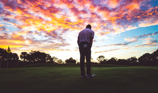 istock Man golfing under stunning sunset sky, putting a golf ball in silhouette 1353063867