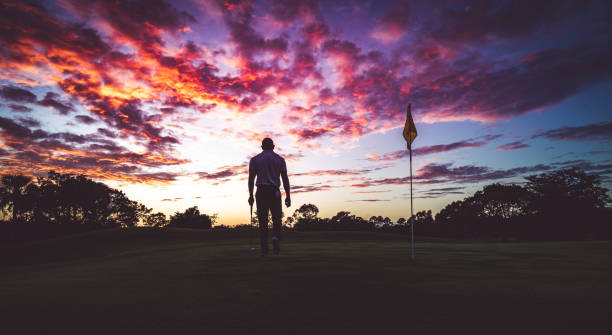 Man golfing under stunning sunset sky, walking the green in silhouette