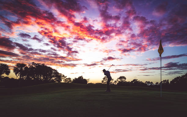 istock Man golfing under stunning sunset sky, taking a swing in silhouette 1353064004