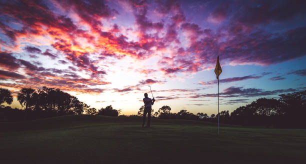 istock Man golfing under stunning sunset sky, taking a swing in silhouette 1353064078