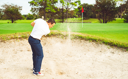 Golf ball tee explode from sand bunker. Golfer hit ball with club to sand explosion to summer sky. Golf club hit ball tee in sand wedge bunker explosion. Blue sky background isolated freeze motion