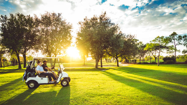 Two male golfers drive golf cart on scenic idyllic golf course playing a round of golf with sunflare stock photo