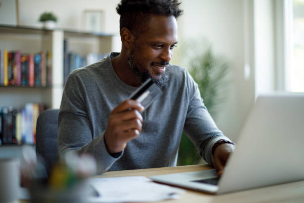 istock Young smiling man using credit card and laptop for shopping online 1353067942