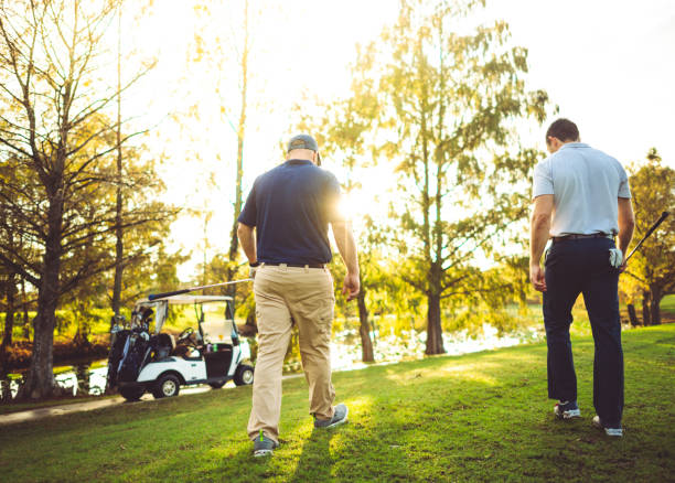 istock Two  golfers walking on a golf course together toward golf cart 1353068931