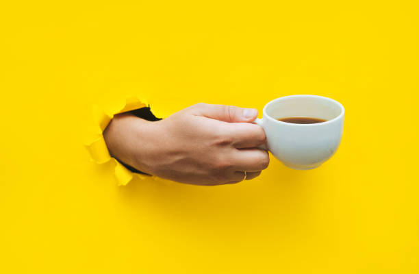 istock A right man's hand holds a white cup with coffee or tea. Torn hole in yellow paper, copy space. The concept of a lunch break at work, lunch. 1353072918