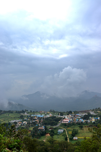 A view from top of the hill station towards the village with mountains in the background and thick clouds hovering everywhere at Devarayana Durga or Devarayanadurga Hills, Tumkur, Karnataka, India.
