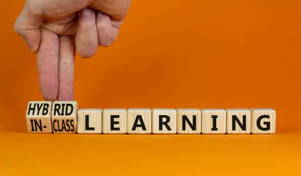 Hybrid or in-class learning symbol. Businessman turns cubes, changes words hybrid learning to in-class learning. Orange background. Education and hybrid or in-class learning concept. Copy space.