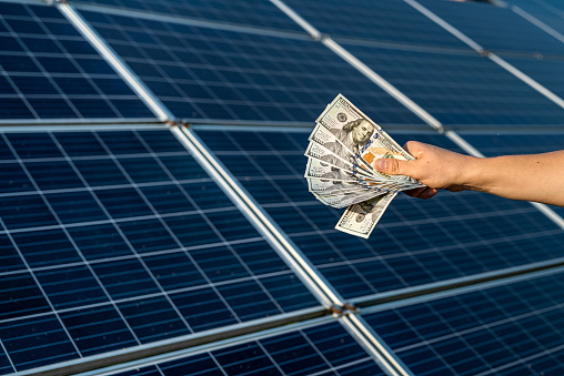 male hand hold hundred dollar at the background of solar station.  concept of generation
