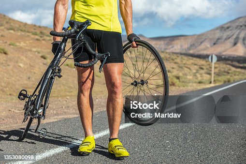 istock Bike repair cyclist man on side of road repair road bicycle problem with wheel. Cycling outdoor athlete biker biking with cycle 1353080098